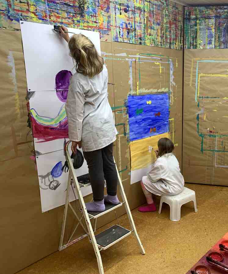 Kind auf Leiter und Kind auf Hocker beim Malen